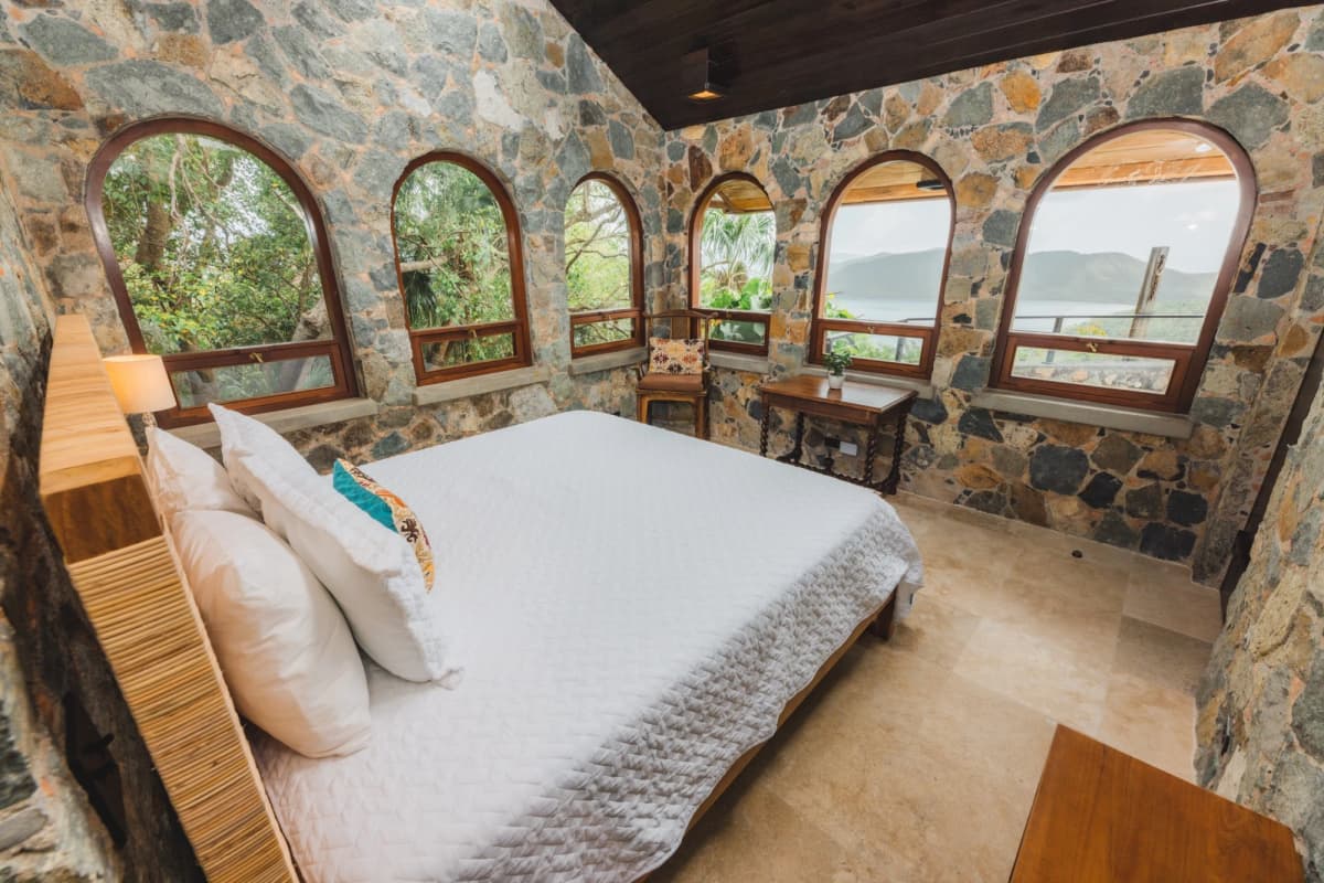 King bedroom suite with ocean views through arched stone windows at Valhalla St John